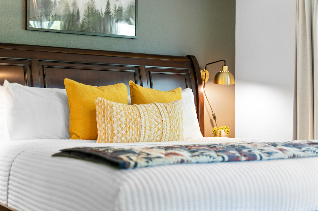 Stylish short-term rental bedroom in Branson, featuring crisp white linens, yellow pillows, and a mountain-inspired blanket.