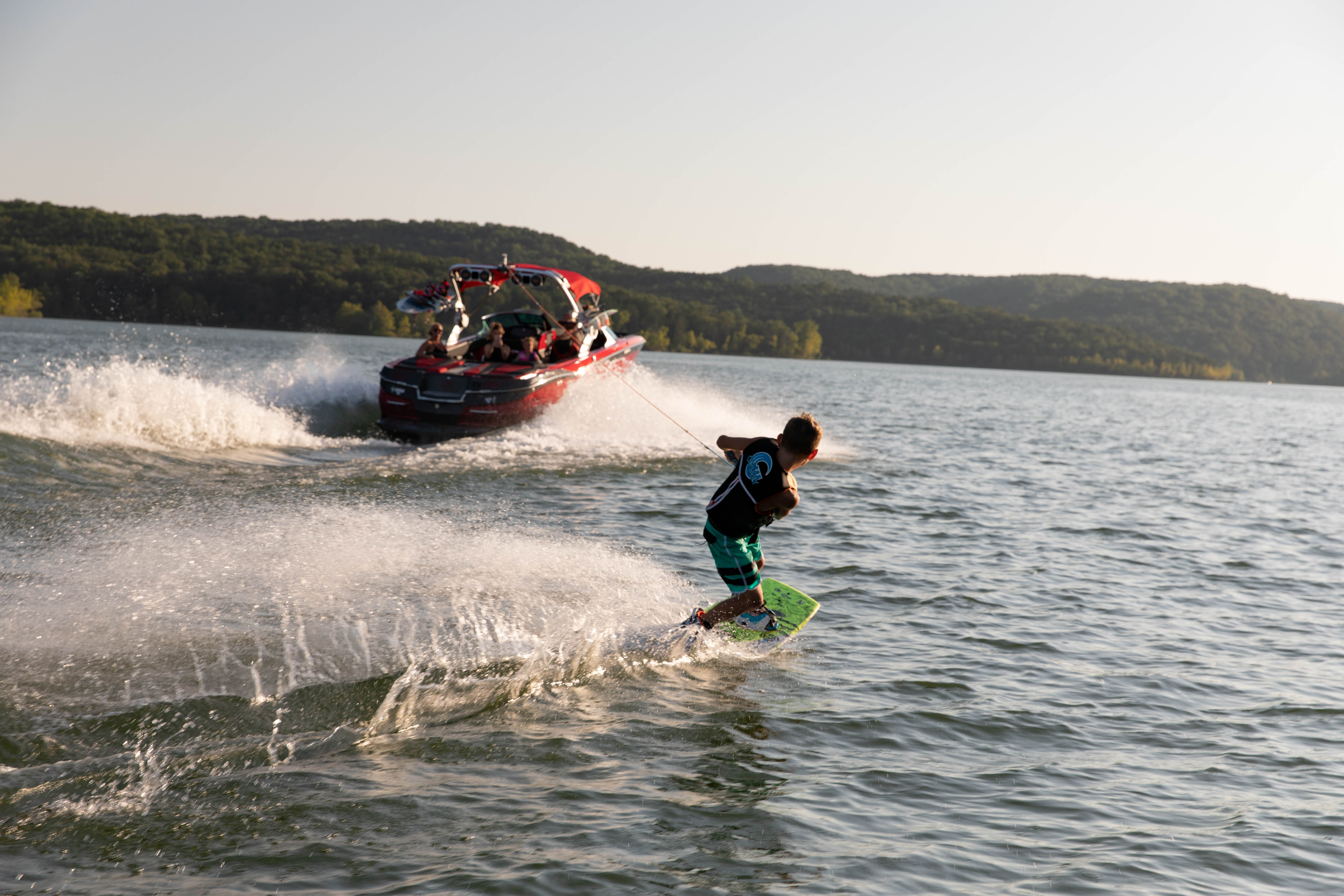 Person wakeboarding behind a red speedboat on Table Rock Lake near Hollister, Missouri, with wooded hills in the background.