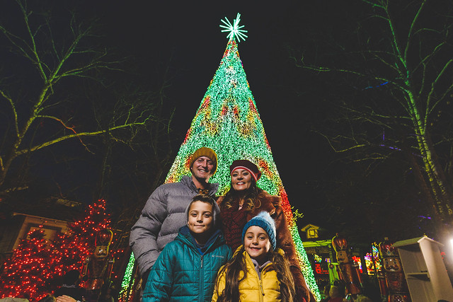 Family posing in front of a large Christmas tree covered in lights at Silver Dollar City in Branson, MO during the holiday season