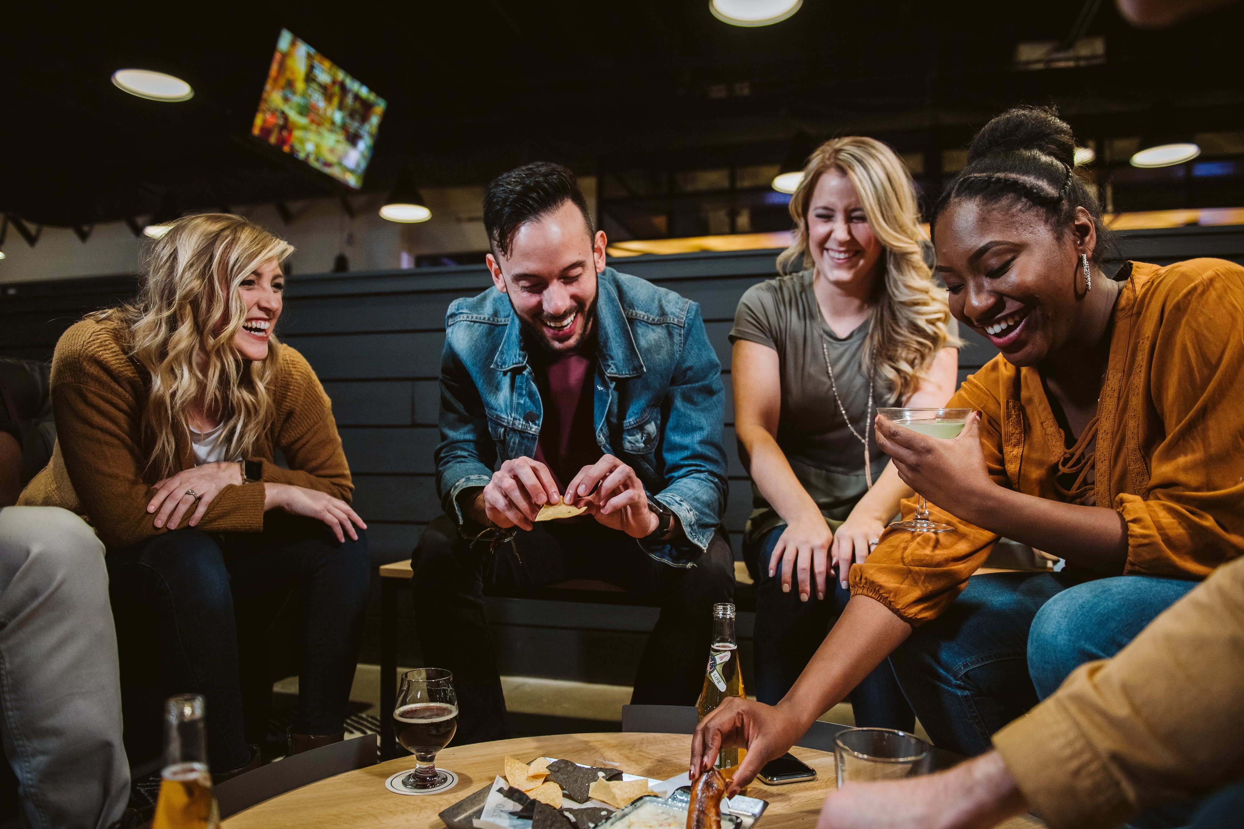 Friends laughing together at a restaurant in Branson, sharing appetizers and drinks around a table in a lively, modern dining setting.