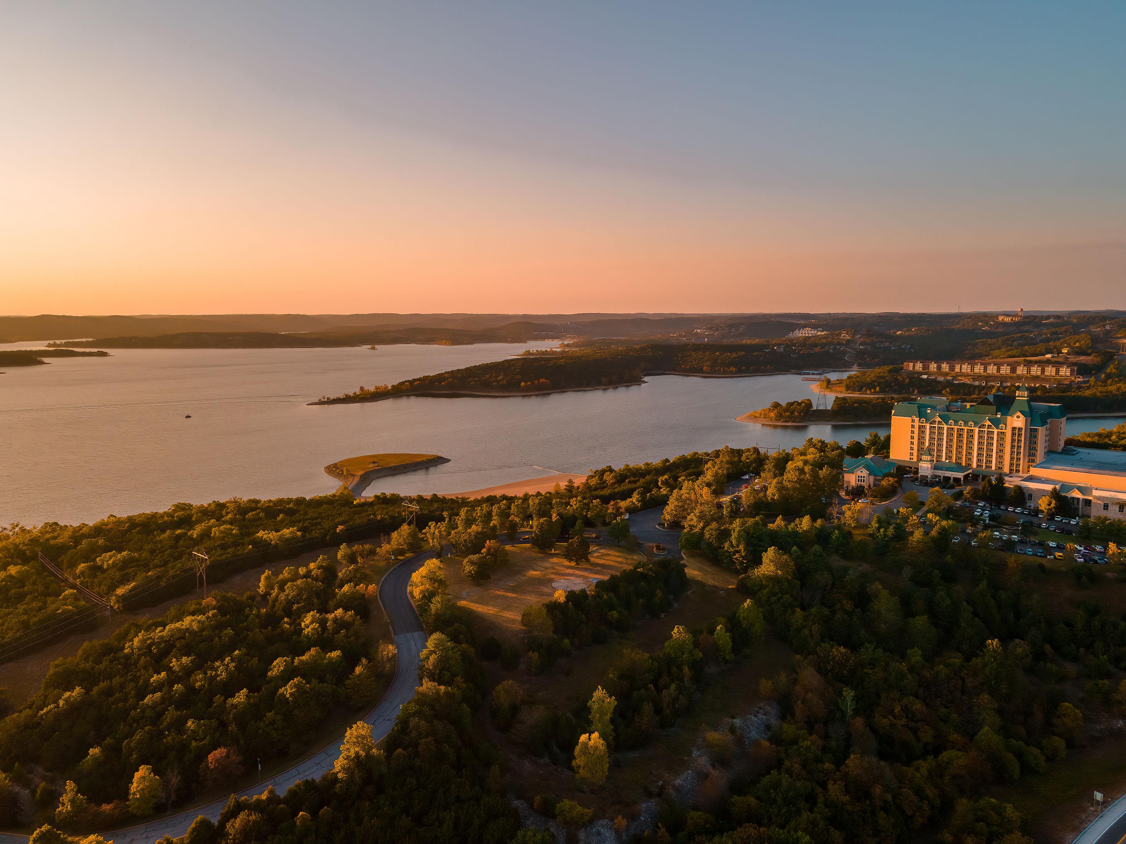 Aerial sunset view of Table Rock Lake near Branson Missouri with wooded hills and lakeside resort buildings along the shoreline.