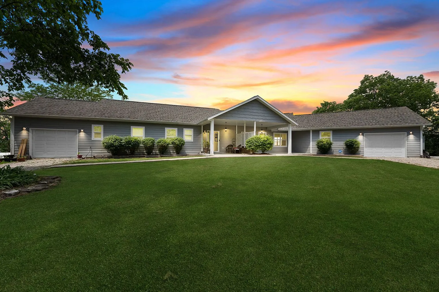 Single-story gray home with dual garages and large front yard at sunset in Branson, Missouri.