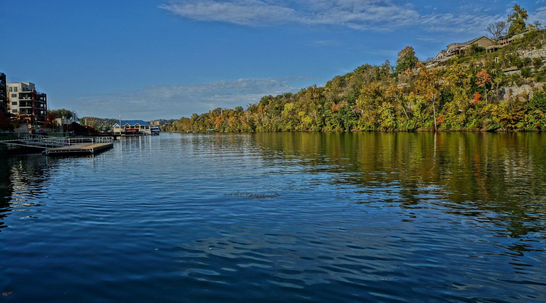 Lake Taneycomo near Branson Landing with calm water, fall foliage along the shoreline, and waterfront buildings in the distance.